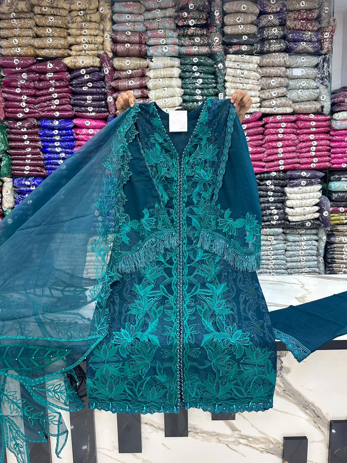Teal lace garment with colorful fabric stacks in the background